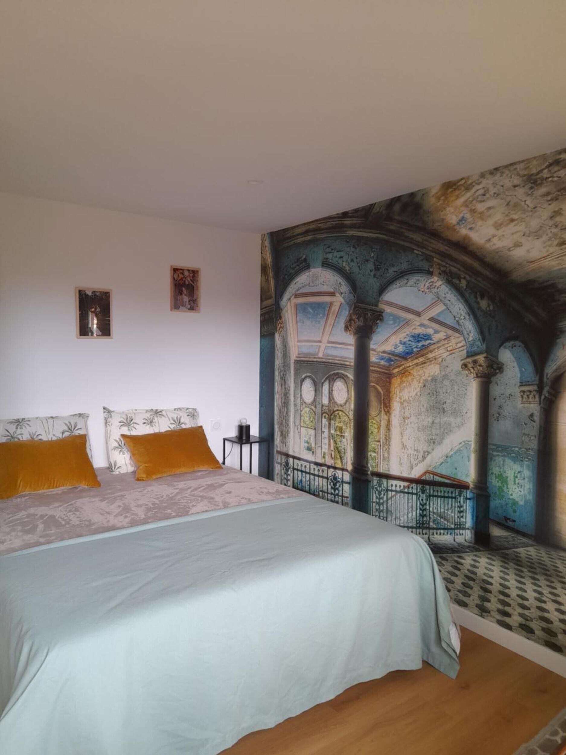 Un dormitori amb un llit gran, dues almoines, una tauleta de nit i un mural a la paret.