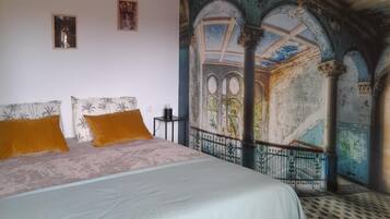Un dormitori amb un llit gran, dues almoines, una tauleta de nit i un mural a la paret.