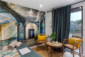 A room with a mural, a bed, a table with a plant, and a chair.