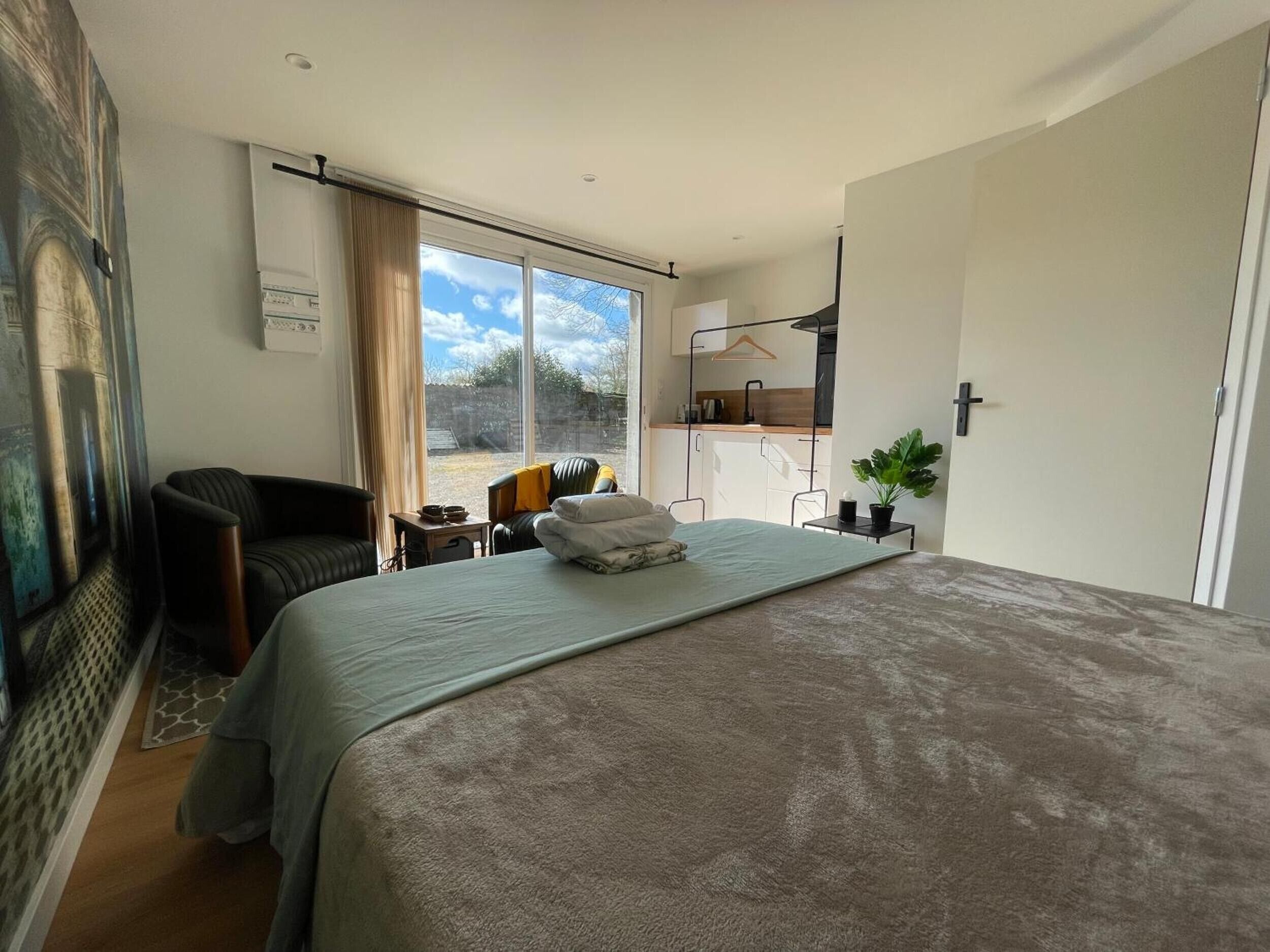 Une chambre à coucher avec un lit, une chaise, une petite table et une vue sur l’extérieur.