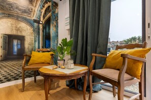 A room with a view of a cityscape, a wooden table with a plant, and two chairs with yellow cushions.