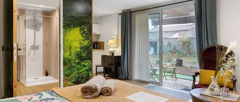 Habitación de hotel con cama, ducha, vista al jardín y zona de comedor.