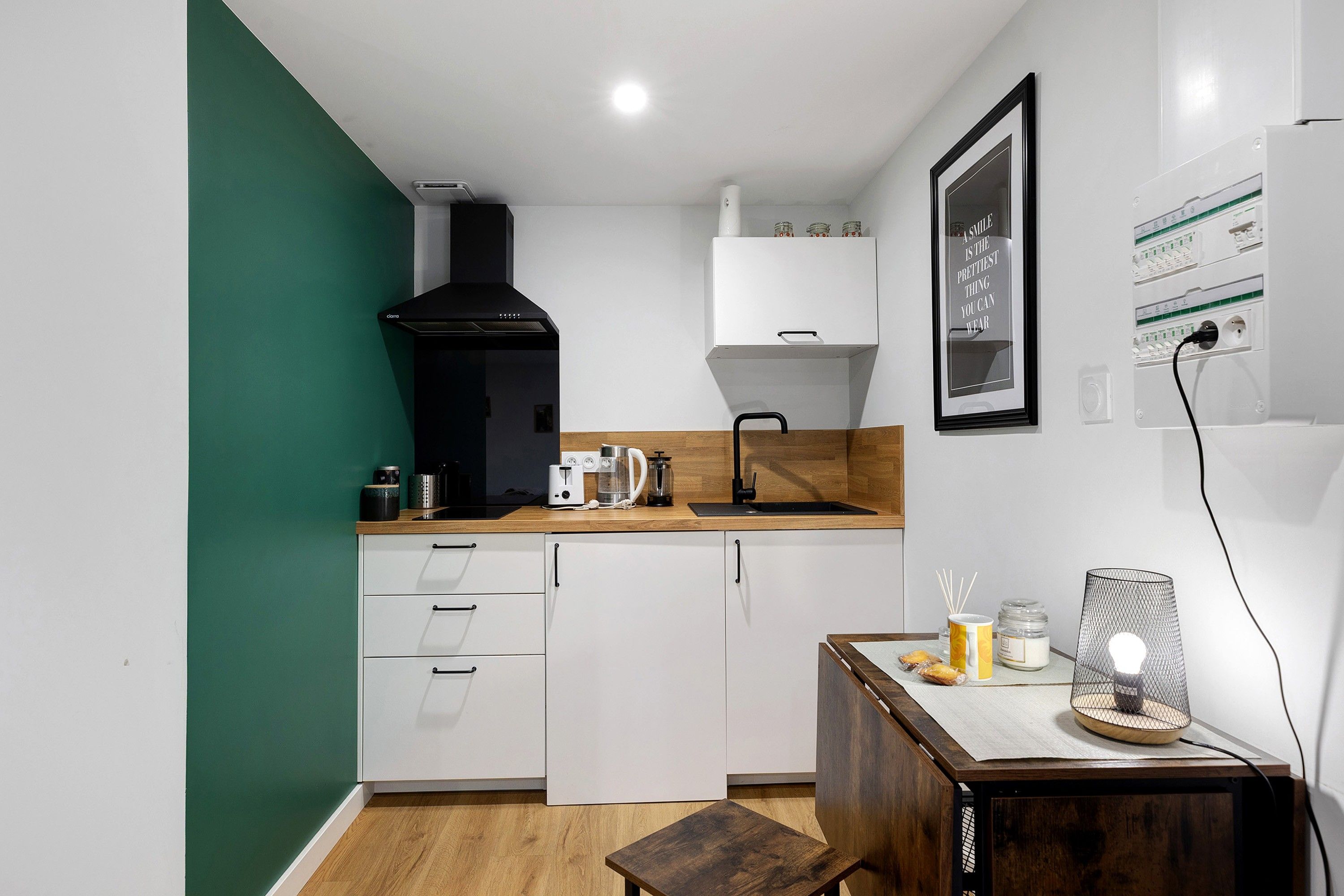 Une cuisine compacte avec des meubles blancs, une hotte noire, un plan de travail en bois et une petite table à manger.