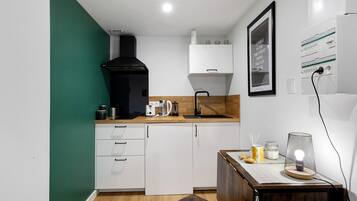 Une cuisine compacte avec des meubles blancs, une hotte noire, un plan de travail en bois et une petite table à manger.