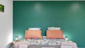 A room with a bed against a green wall, two pillows, a patterned bedspread, and two bedside lamps.
