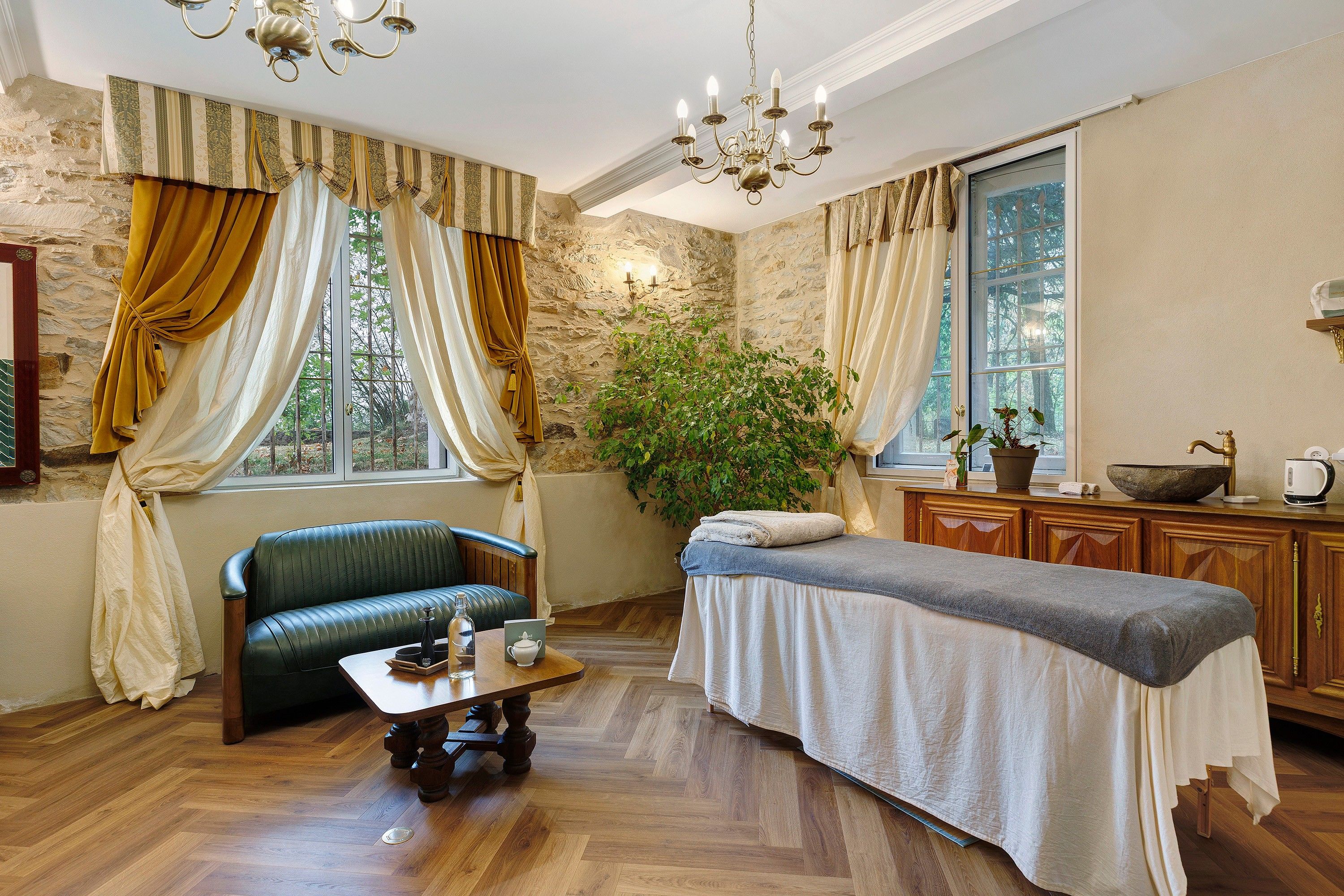 A room with a sofa, a massage table, a wooden cabinet, a potted plant, and a chandelier.