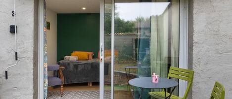 A room with a bed, a chair, a table, and a sliding glass door leading to an outdoor area.