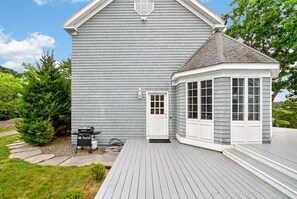 A house with a grey exterior, a white door, and a covered porch area. - Modern Cottage Overlooking Sheepscot River (Boothbay)