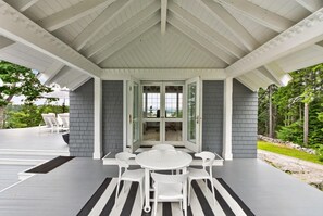 Une terrasse extérieure couverte, avec une table ronde et des chaises, offrant une vue sur le paysage, et une porte donnant accès à un espace intérieur.