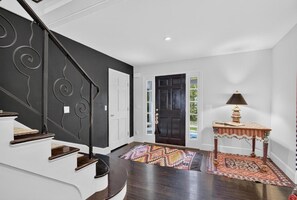 A staircase with a black railing leading to a white door, a patterned rug on the floor, and a table with a lamp. - Modern Cottage Overlooking Sheepscot River (Boothbay)