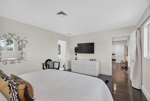 A bedroom with a large bed, a dresser, a TV, and a mirror. - Modern Cottage Overlooking Sheepscot River (Boothbay)