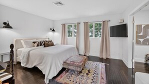 Ein Schlafzimmer mit einem Bett, einem Fernseher, einem Fenster mit Vorhängen und einem gemusterten Teppich.