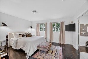 Ein Schlafzimmer mit einem Bett, einem Fernseher, einem Fenster mit Vorhängen und einem gemusterten Teppich.