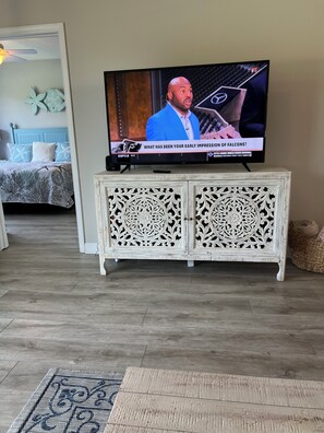 A television on a white cabinet with intricate carvings, a bed with a blue headboard and patterned bedding, and a wooden floor. - Golf and Beach Condo!! Sleeps 8! Labor Day Special! Resort amenities! (North Myrtle Beach)