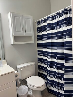 A bathroom with a white toilet, a white cabinet, and a striped shower curtain. - Golf and Beach Condo!! Sleeps 8! Labor Day Special! Resort amenities! (North Myrtle Beach)