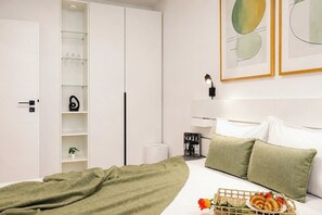 A bedroom with a bed, pillows, a bedside table, a lamp, a wardrobe, and a framed picture on the wall.
