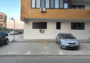 A parking area with marked spaces, a building with air conditioning units, and a street lamp.