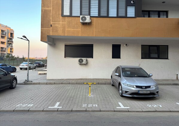 Un espace de stationnement avec des places délimitées, un bâtiment équipé de climatiseurs et un lampadaire.