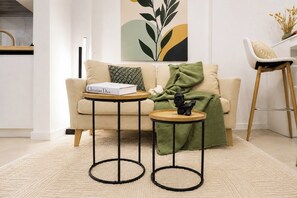 A living room with a sofa, two side tables, a book, a decorative sculpture, and a painting on the wall.