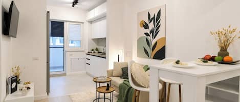 Une cuisine moderne avec des meubles blancs, un coin repas avec une table et des chaises blanches, et un salon avec un canapé et une table basse.