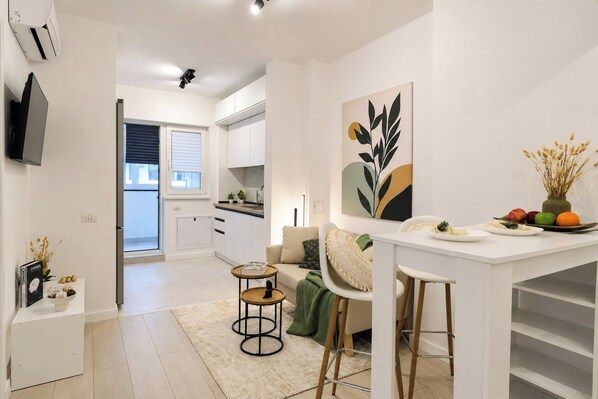 A modern kitchen with white cabinets, a dining area with a white table and chairs, and a living room with a sofa and a coffee table.