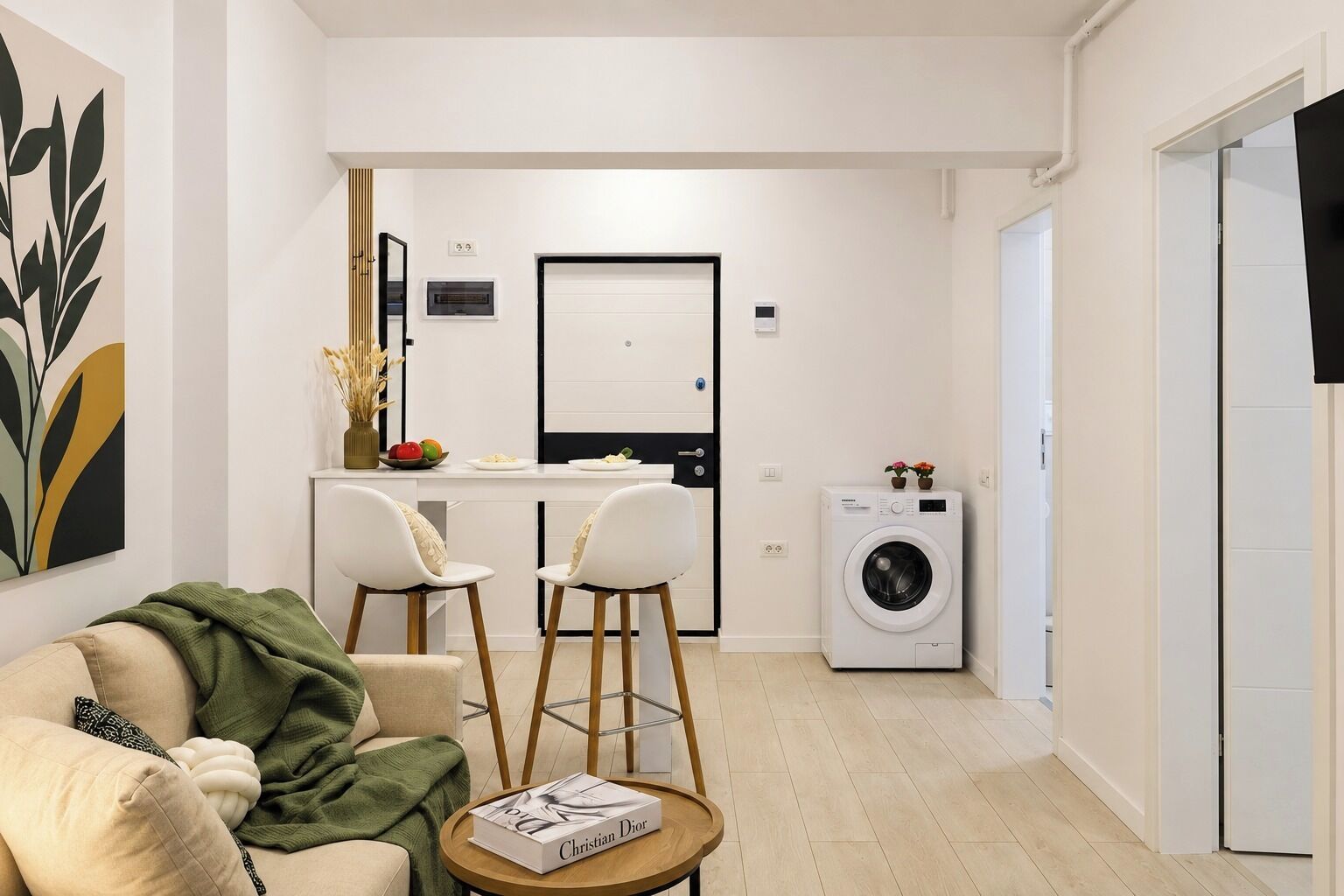 A compact living space with a sofa, two chairs, a coffee table, a washing machine, and a small kitchen area with a fridge and a microwave.