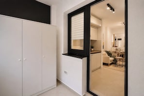 Un interior moderno con un armario, una ventana con persianas y una vista parcial de una sala de estar con sofá y mesa.