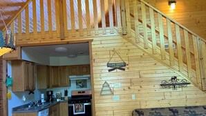 A wooden interior with a staircase leading to a loft area, a kitchen with wooden cabinets, and a dining area with a table and chairs.