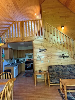 A wooden interior with a staircase leading to a loft area, a kitchen with wooden cabinets, and a dining area with a table and chairs.