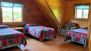 A cozy attic bedroom with three beds, wooden floors, and a sloped ceiling with a ceiling fan.