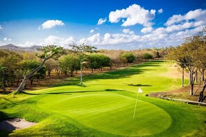 A golf course with a flagstick, trees, and a clear sky. - Eco Casita 1.8 in Hacienda Iguana (Tola)