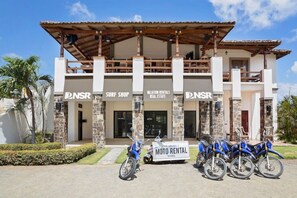 A building with signage for a surf shop, vacation rentals, and real estate. There are motorcycles parked in front. - Eco Casita 1.8 in Hacienda Iguana (Tola)