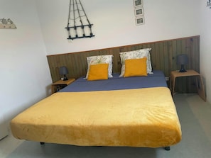 Una cama con colcha azul y amarilla, dos almohadas, cabecero de madera y dos mesitas de noche con lámparas.