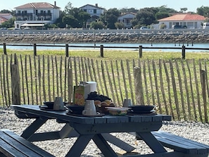A picnic table with food and drinks, set against a backdrop of a river and houses.