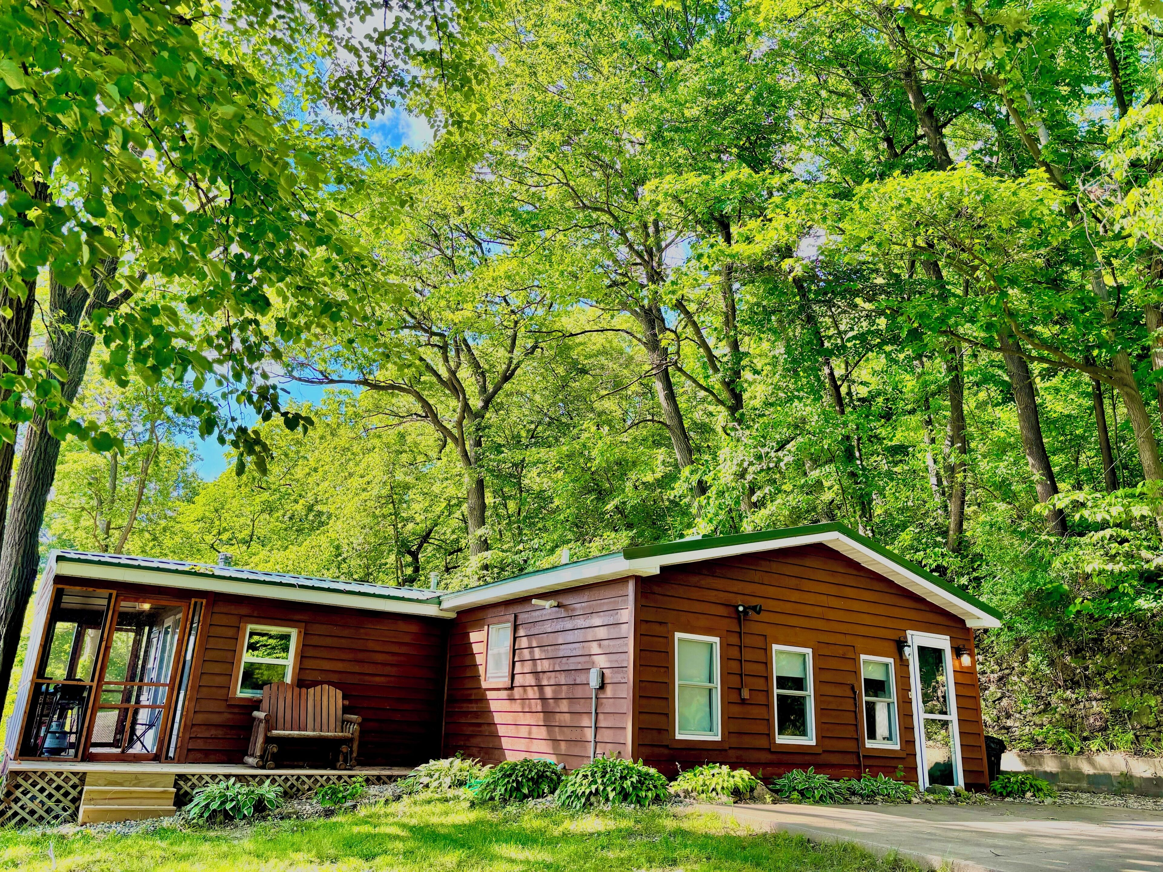 A wooden cabin with a porch, surrounded by dense green trees.