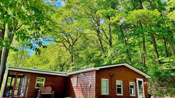 A wooden cabin with a porch, surrounded by dense green trees.