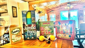 Une table en bois sur laquelle on trouve divers jeux de société, notamment « Jumbo Pong », « Apples to Apples Junior » et « Simpsons Ultimate Trivia Game ».