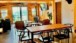 Un intérieur rustique avec un plafond en bois, un coin repas comprenant une table et des chaises, une cheminée et un téléviseur fixé au mur.