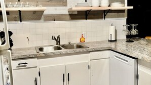 Une cuisine avec des armoires blanches, un comptoir en granit et des étagères en bois au-dessus.