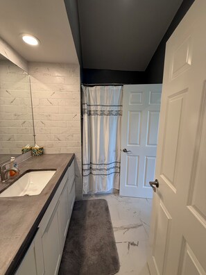 Un baño con lavamanos blanco, toallero, cortina de ducha y puerta.
