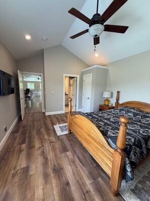 Un dormitorio con cama de madera, ventilador de techo y vista al área de estar contigua.