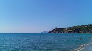 A coastal landscape with a clear sky, calm sea, and a rocky hill with buildings. - Villa Carra (Ansedonia)