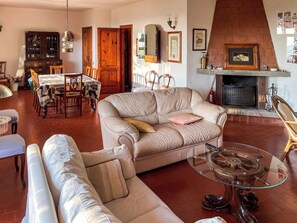 A living room with a beige sofa, a glass coffee table, and a fireplace. - Villa Carra (Ansedonia)