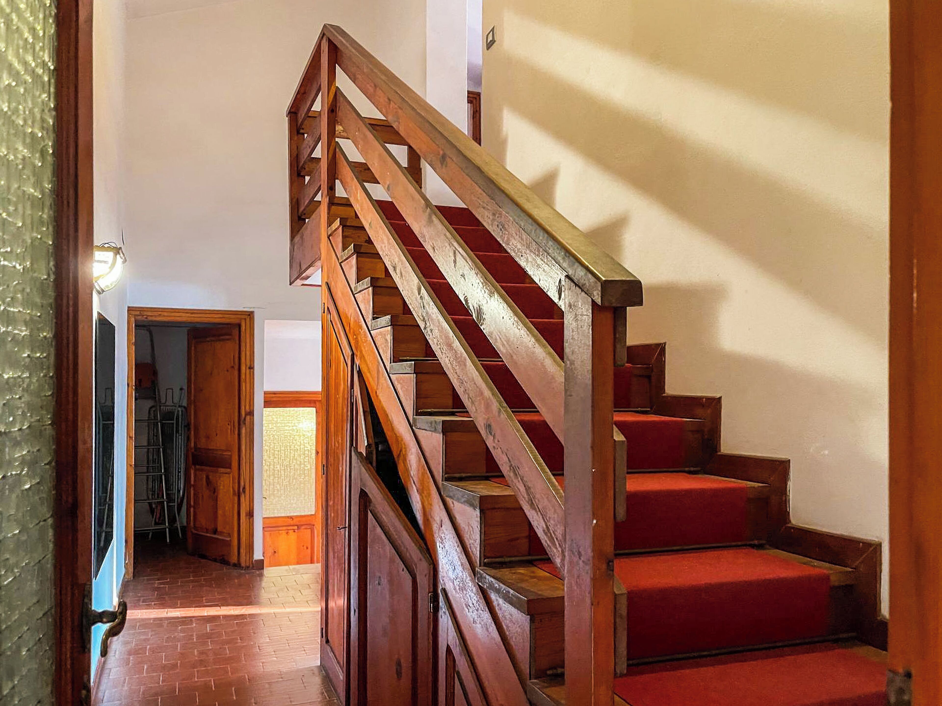 A wooden staircase with red carpeted steps leading to an upper floor.
