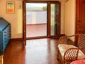 A room with a sliding glass door leading to a terrace, a wicker chair, and a blue cabinet. - Villa Carra - Ansedonia (Ansedonia)