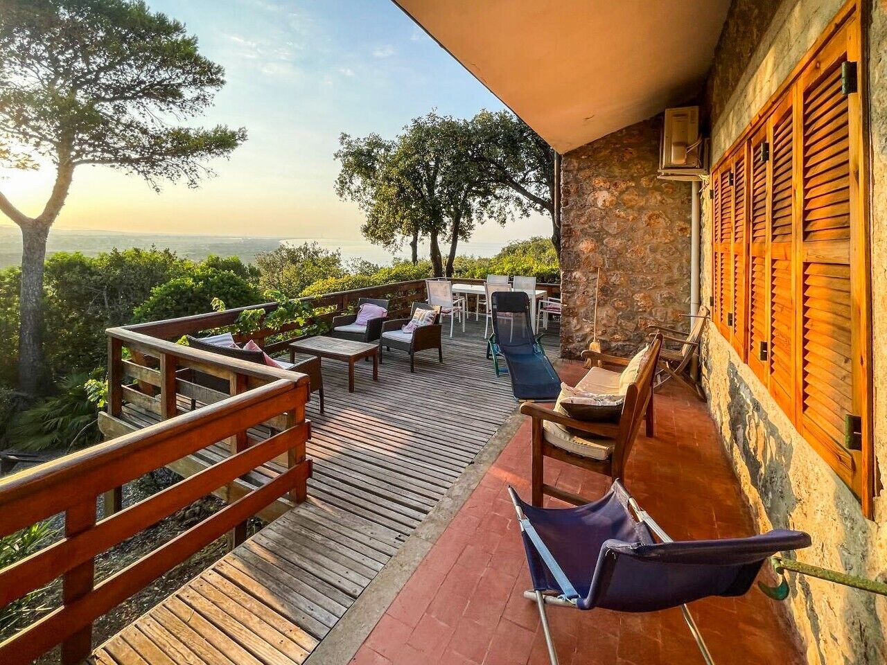 A wooden deck with outdoor furniture, a stone wall, and a view of the landscape.