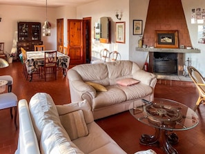 A cozy living room with a fireplace, leather sofas, a dining area with a wooden table, and a glass coffee table. - Villa Carra - Ansedonia (Ansedonia)