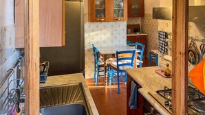 A compact kitchen with a sink, stove, and blue chairs around a table. - Villa Carra - Ansedonia (Ansedonia)