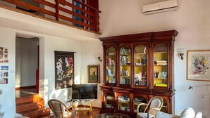 A spacious living area with a high ceiling, a wooden staircase, a flat-screen TV, a large wooden cabinet, and a dining table. - Villa Carra - Ansedonia (Ansedonia)