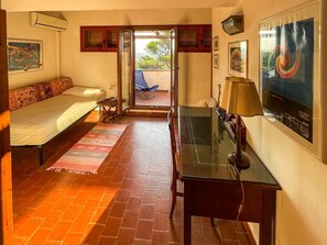 Ein Zimmer mit Bett, Schreibtisch, Sessel, Sofa, Fernseher und Blick ins Freie.